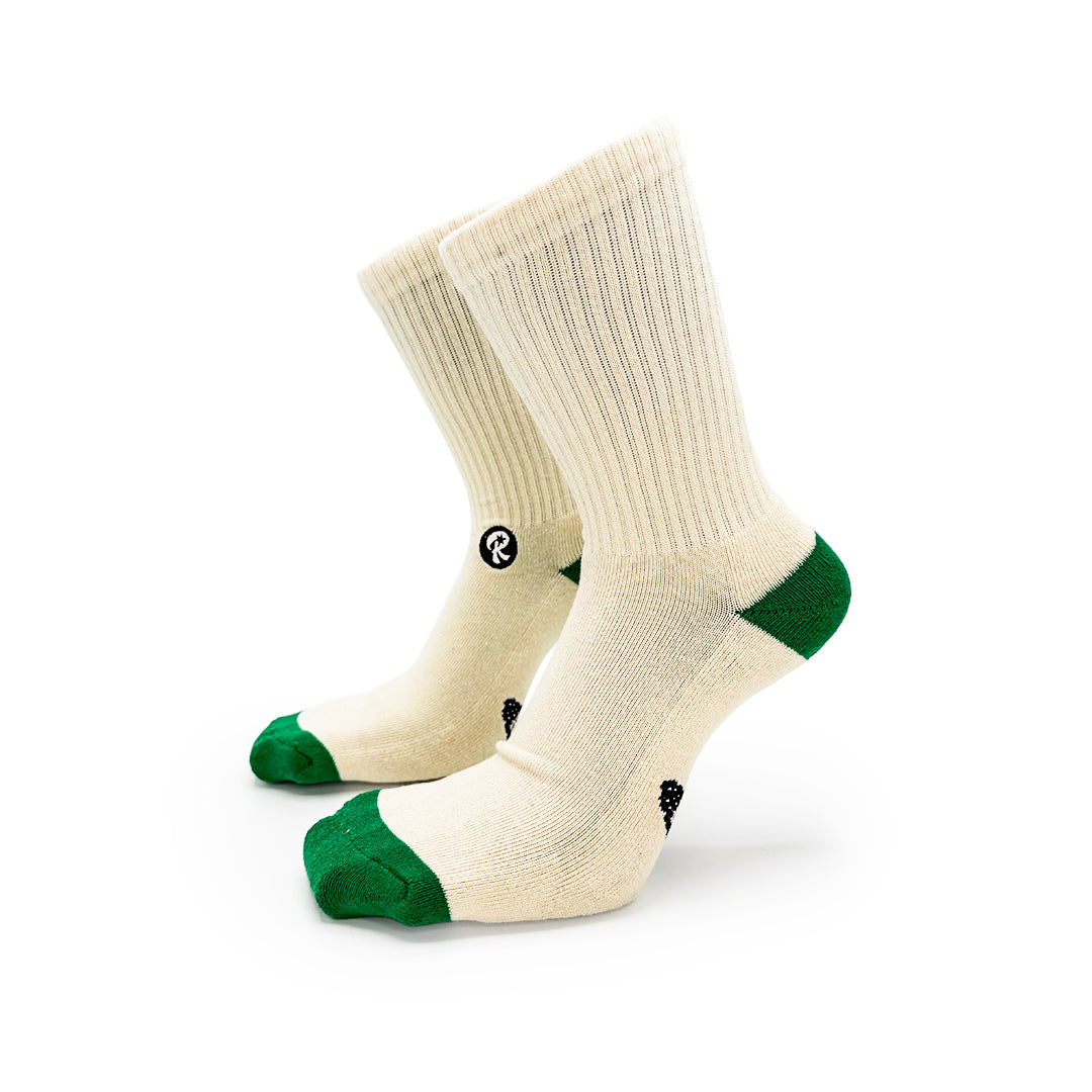 A pair of crew socks in cream with green toes and heels featuring small black 'RELISH' logo graphics, shown on a white background.