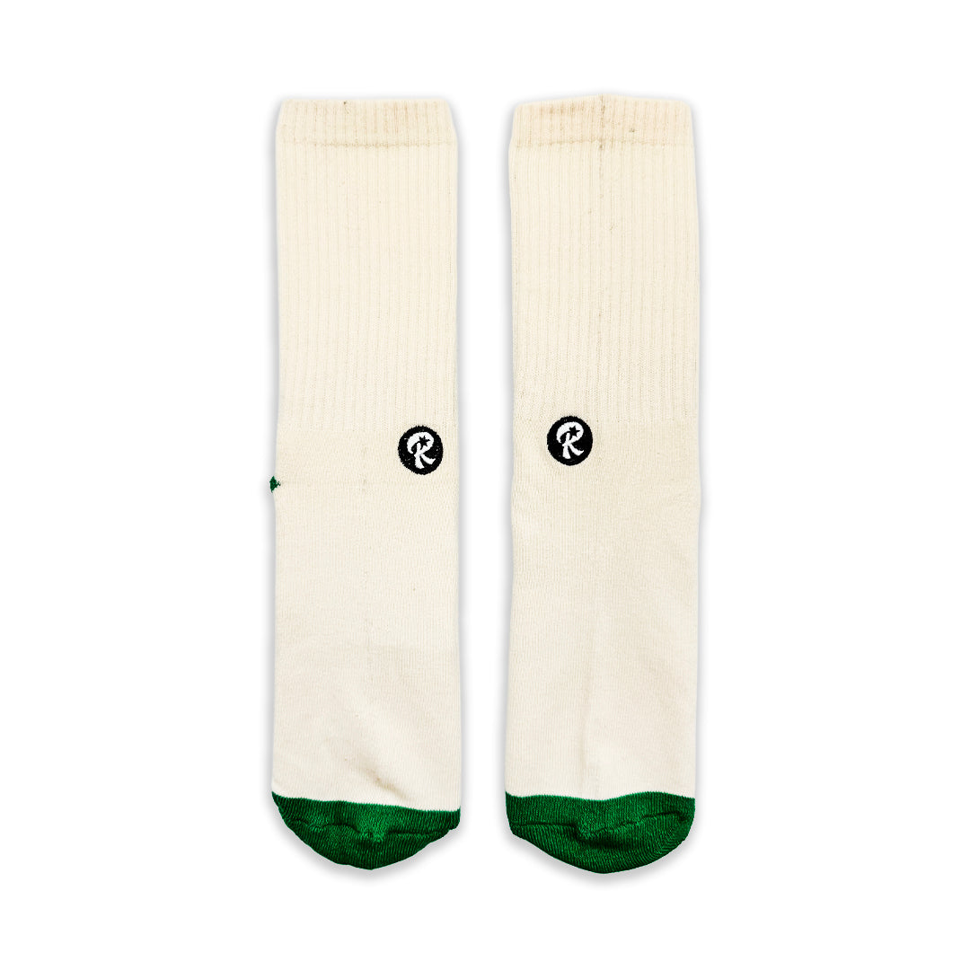 A pair of off-white crew socks with dark green toes and heels, featuring a small black circular logo with a white 'R' for 'RELISH' on each sock, displayed flat against a white background.